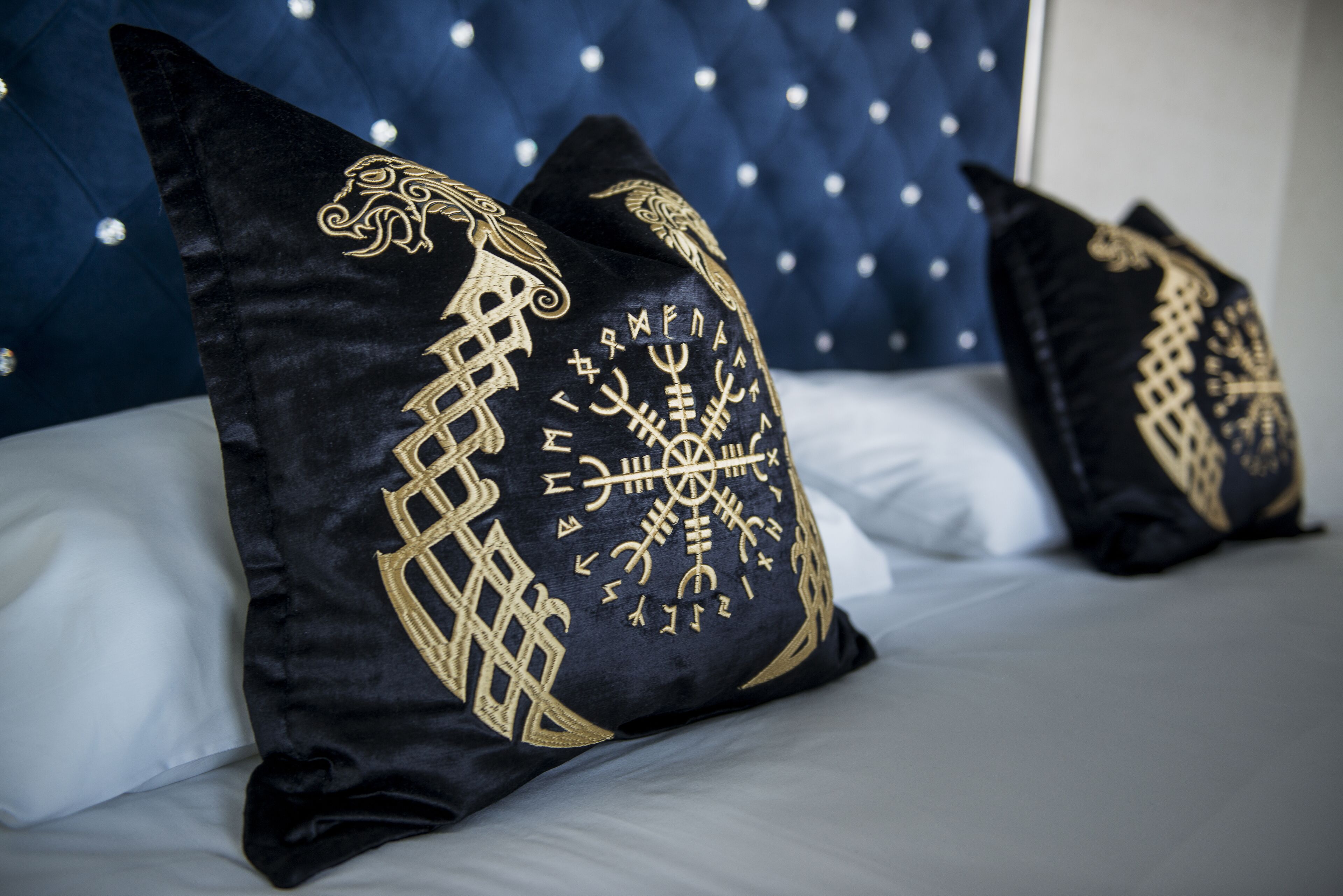 A bed with black pillows featuring gold embroidery and a blue headboard.