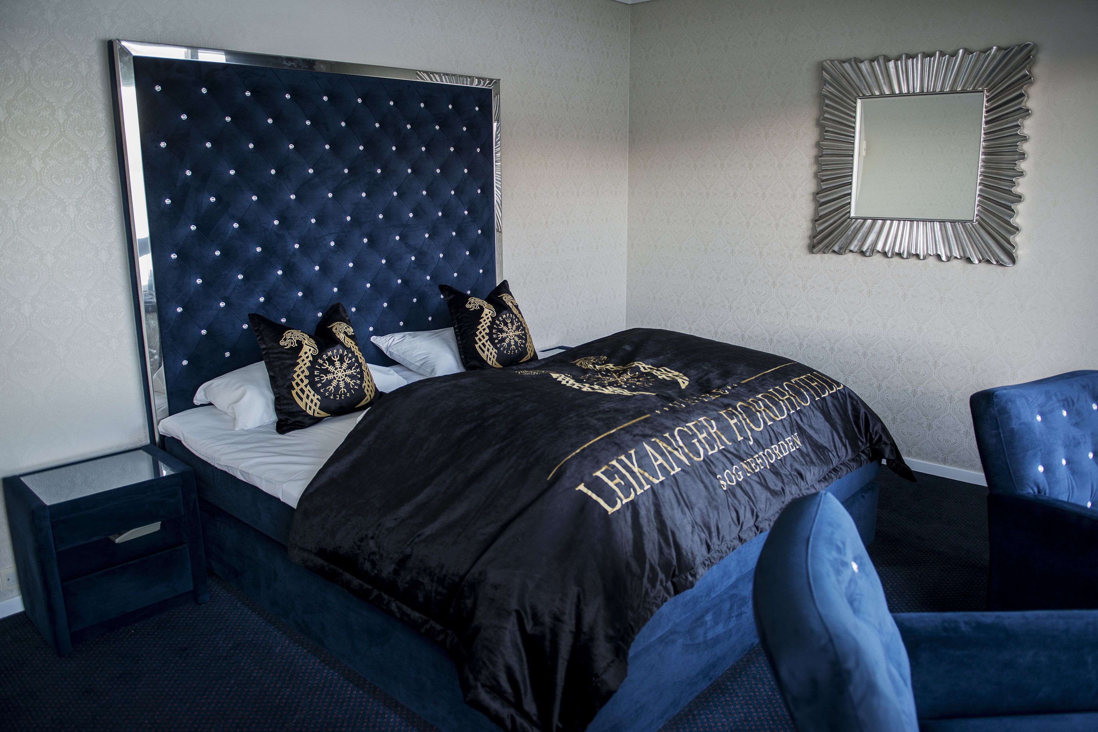 Habitación de hotel con una cama grande, un cabecero con diseño de estrellas, un espejo en la pared y una silla azul.