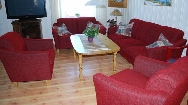 A living room with a red sofa set, a wooden coffee table, a television on a stand, and a painting on the wall. - Fjordhotell (Stryn)