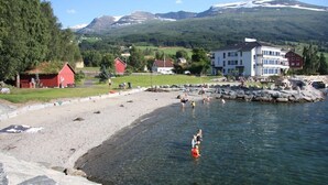 A coastal area with clear waters, a sandy beach, and buildings in the background. - Fjordhotell (Stryn)