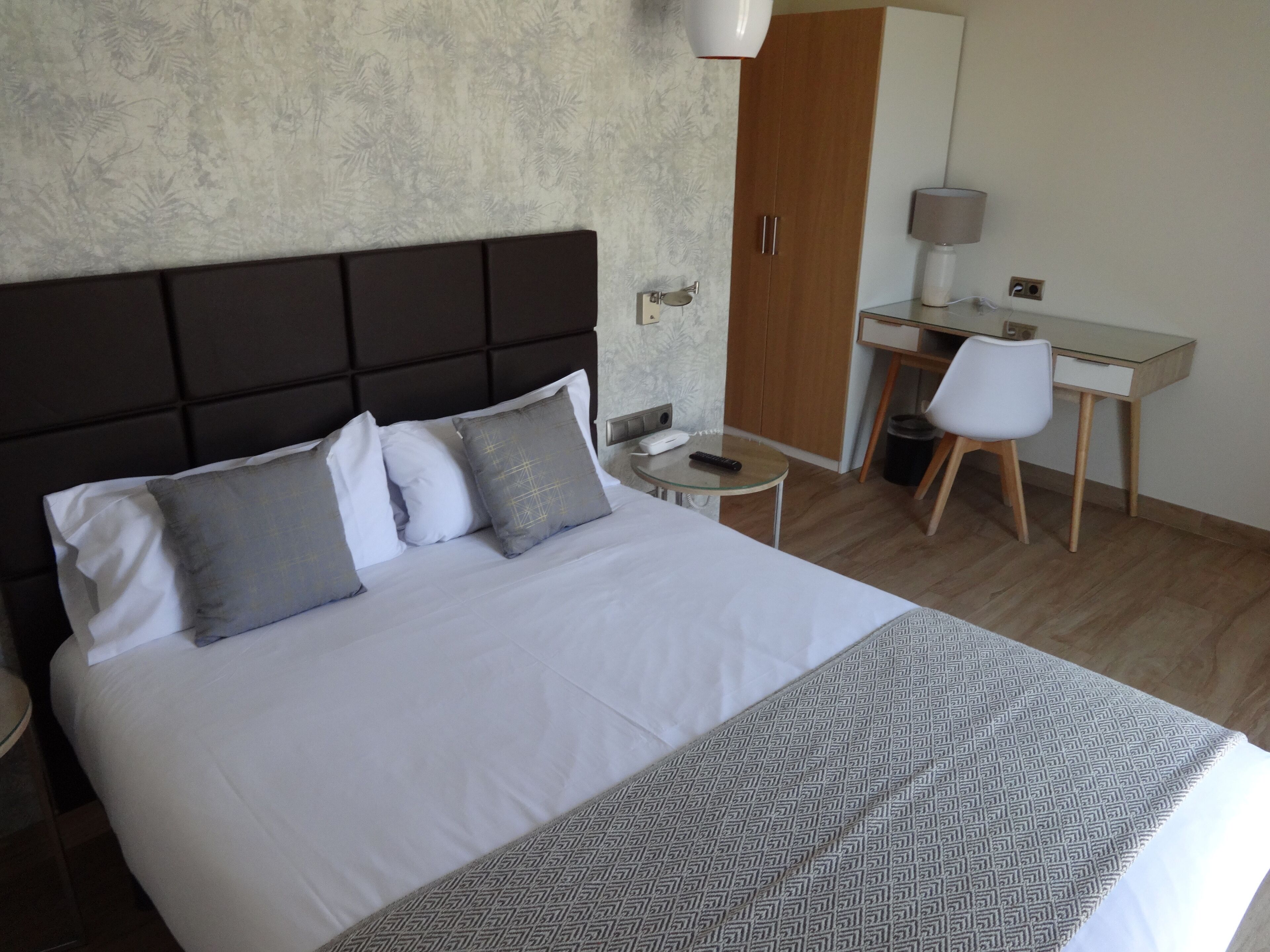 A hotel room with a large bed, a desk, a chair, a lamp, and a wardrobe.