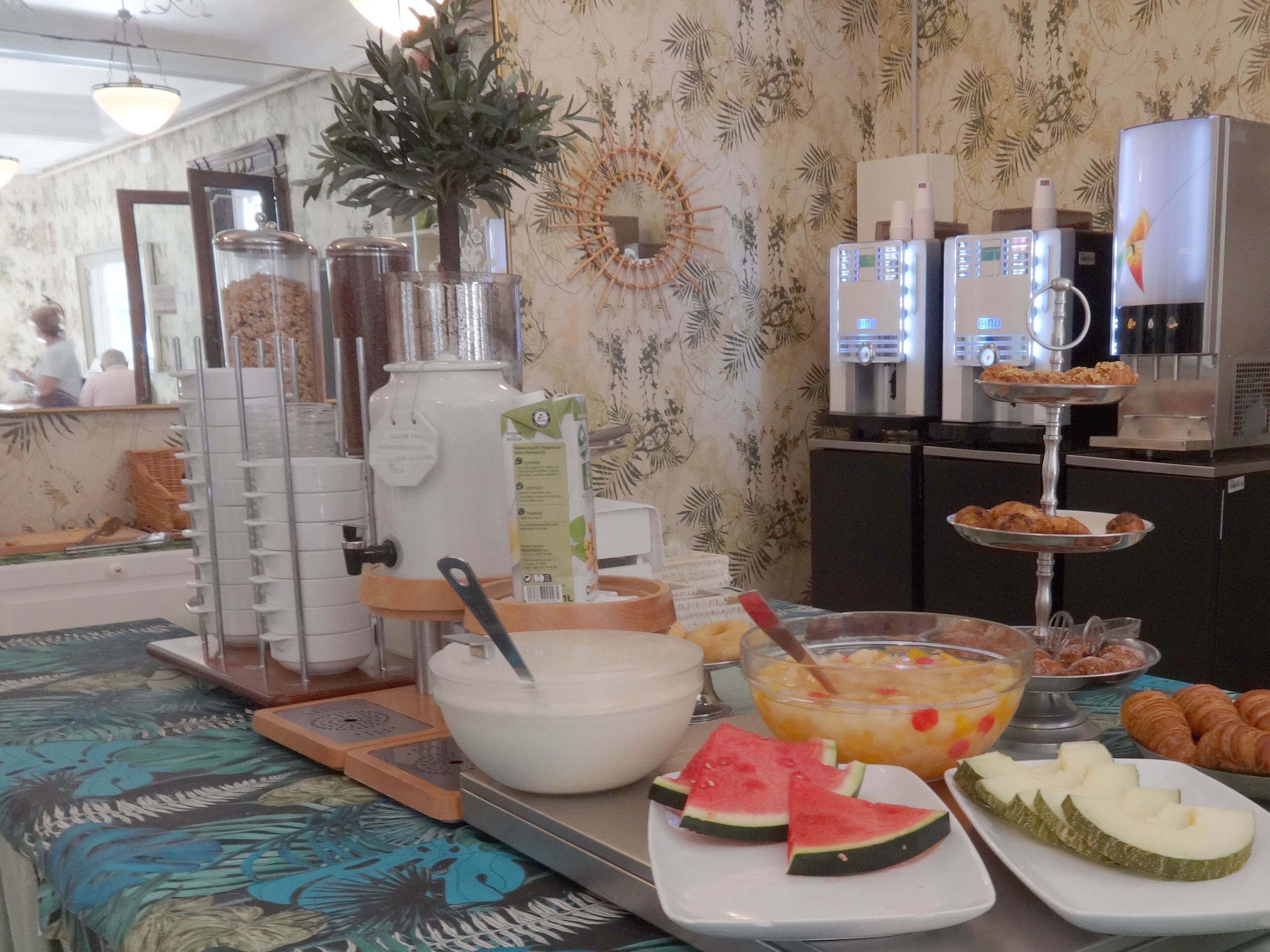 A buffet setup with various food items, a coffee machine, and a decorative plant.
