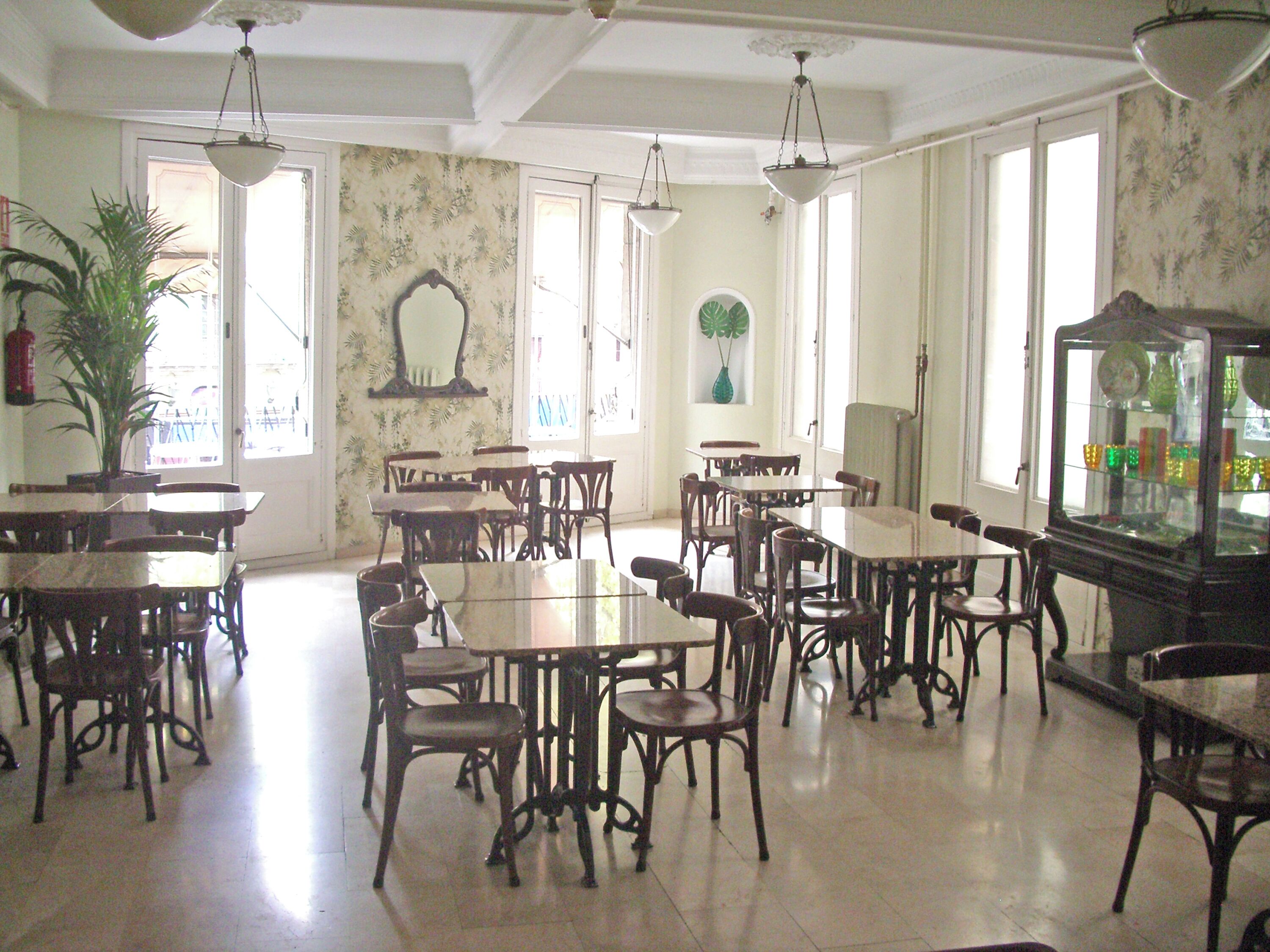 A dining area with multiple tables and chairs, large windows, and a decorative cabinet.