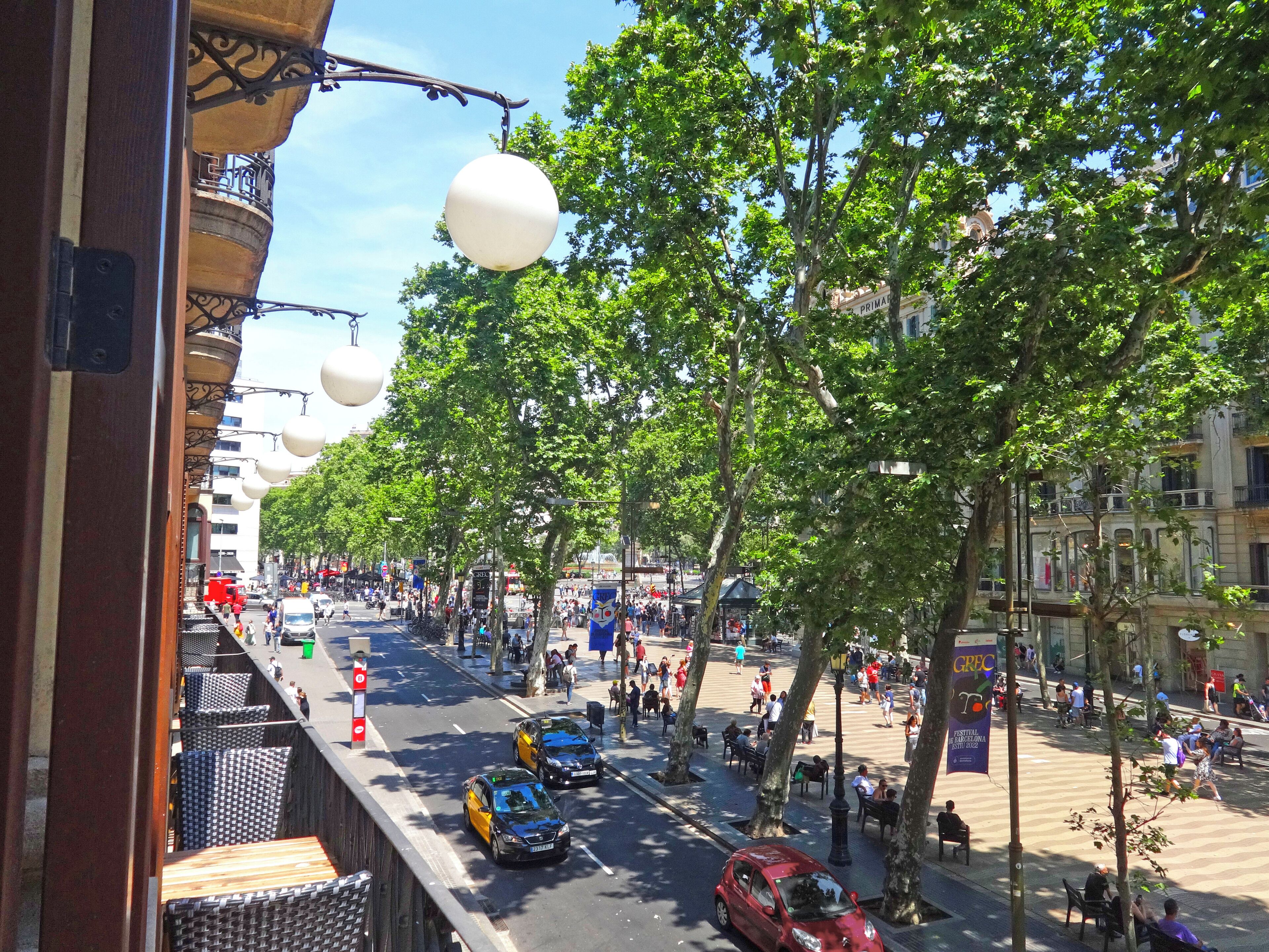 A busy urban street lined with trees and street lamps, with pedestrians and vehicles.