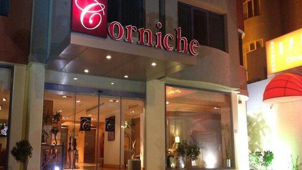 The exterior of a hotel named 'Orniche' with a prominent red sign, large glass windows, and a modern architectural design. - Le Royal Corniche (Salmiya)