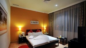 A hotel room with a bed, two bedside tables, a TV, and a large window with curtains. - Le Royal Corniche (Salmiya)