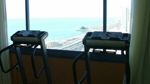 Two exercise bikes positioned by a window with a view of a coastal cityscape. - Le Royal Corniche (Salmiya)