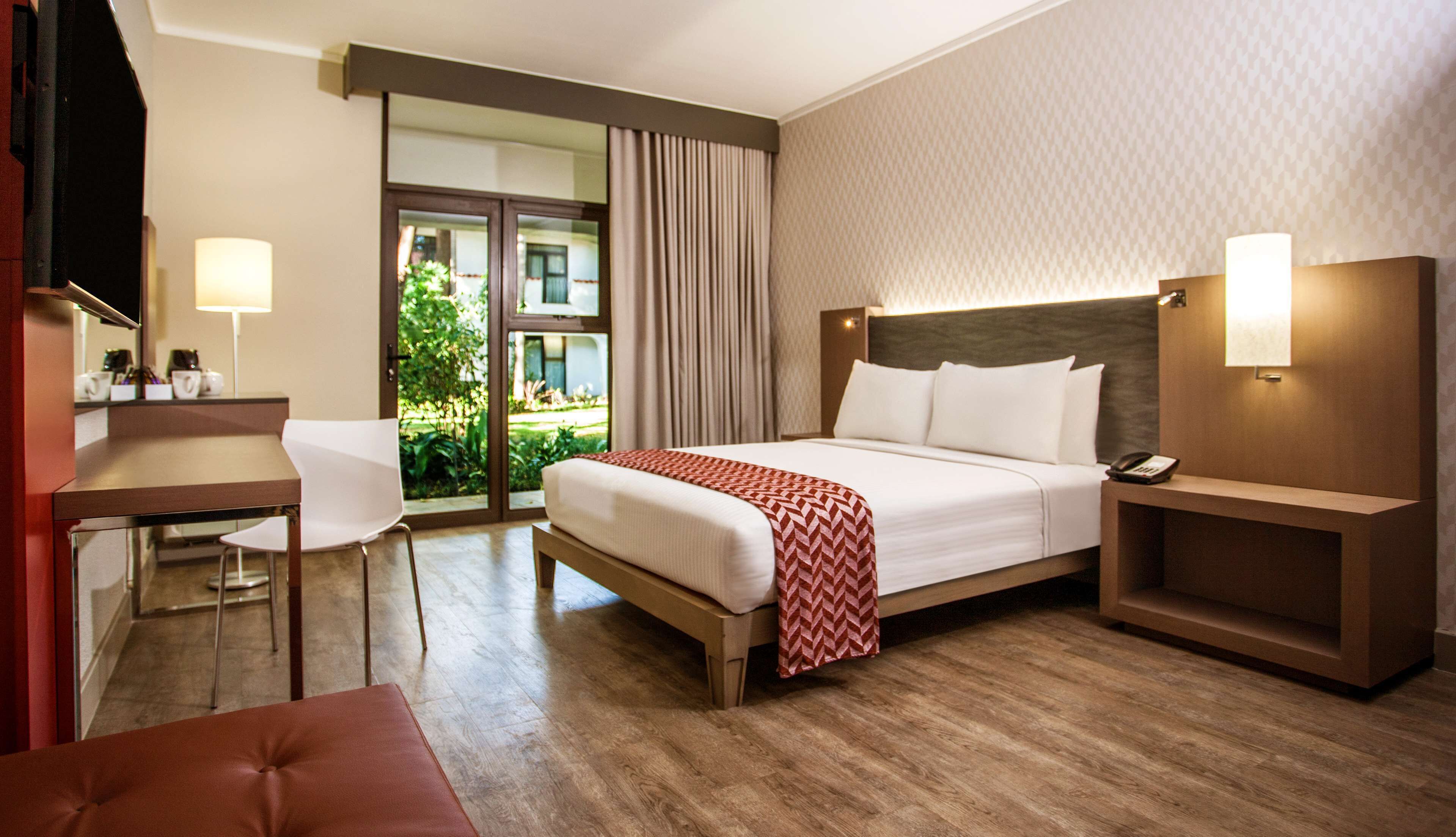Ein Hotelzimmer mit Bett, Nachttisch, Stuhl, Schreibtisch und Blick ins Freie.