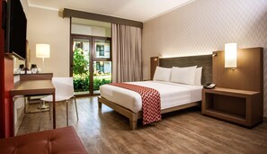 Een hotelkamer met een bed, nachtkastje, stoel, bureau en uitzicht op het omliggende landschap.