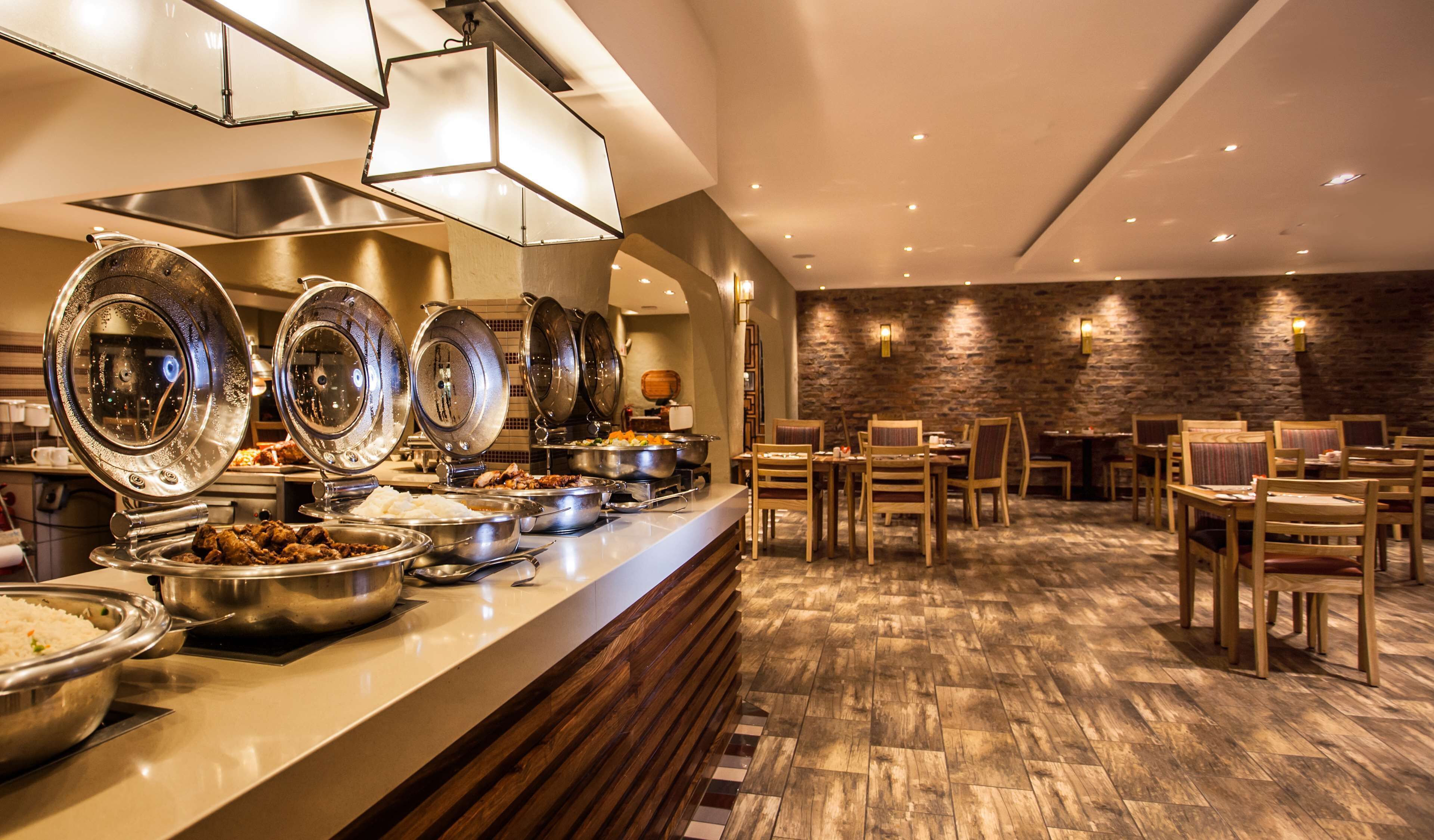 A buffet area with multiple serving stations, wooden chairs, and a stone wall in the background.