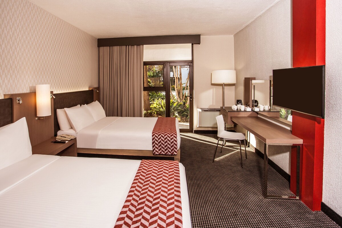 Een hotelkamer met twee bedden, een bureau, een stoel, een televisie en een raam met gordijnen.