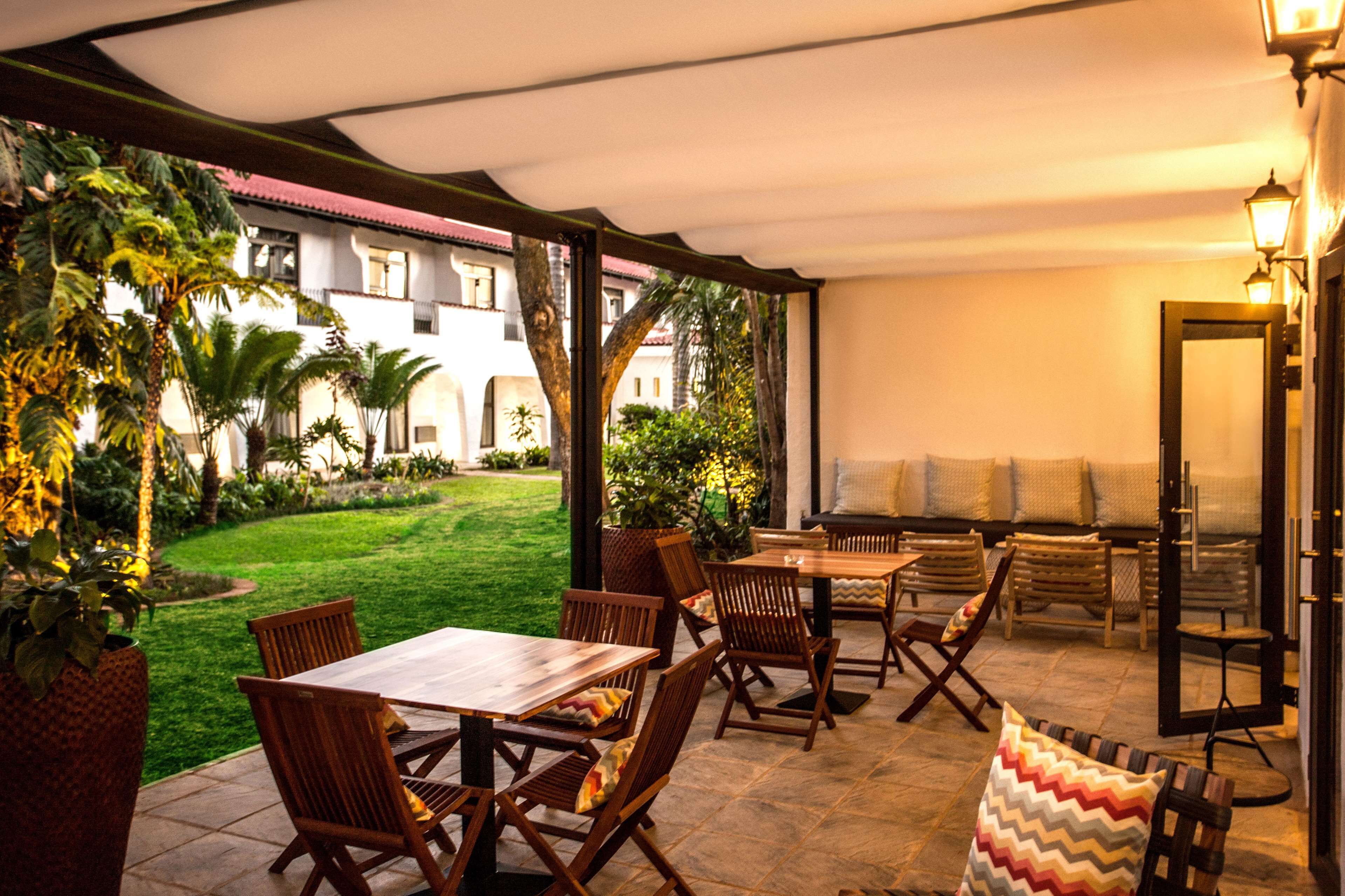Eine Außenpatio-Terrasse mit Holzmöbeln, einem Grill und Blick auf einen Garten sowie ein Gebäude im Hintergrund.