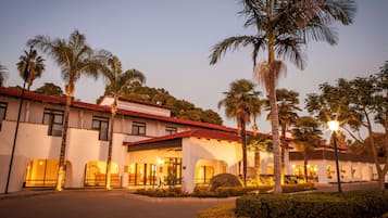 A hotel with a red-tiled roof, palm trees, and well-lit entrance.