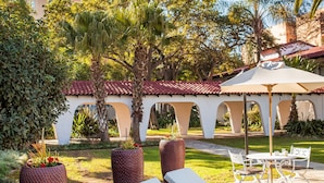 Un patio con sillones de descanso, una pérgola y un camino que lleva a un edificio con techo de tejas rojas.