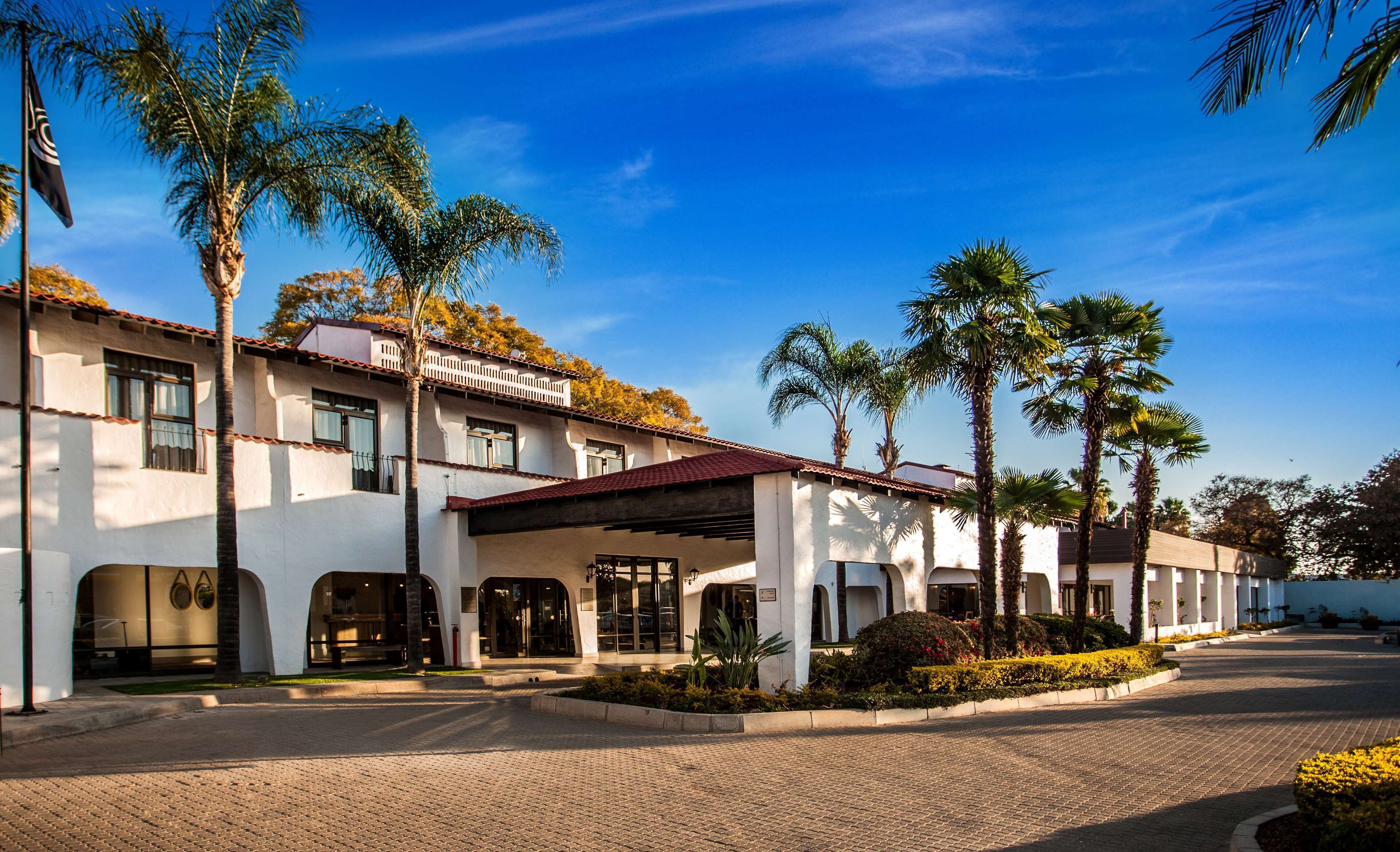 A hotel with a white facade, multiple balconies, and palm trees.