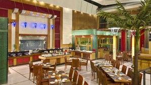 Un restaurante espacioso con varias mesas y sillas, una barra central y una planta grande en el centro.