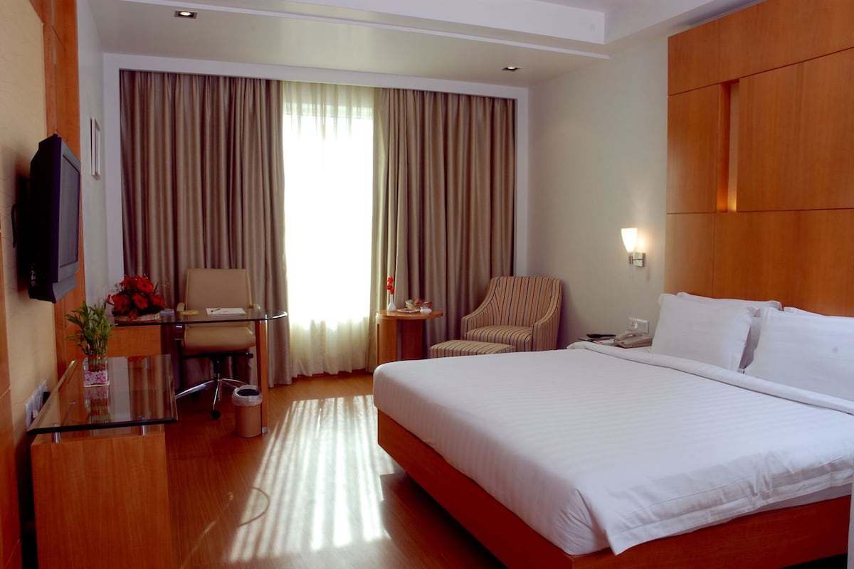 A hotel room with a large bed, a desk with a chair, a television, and a window with curtains.