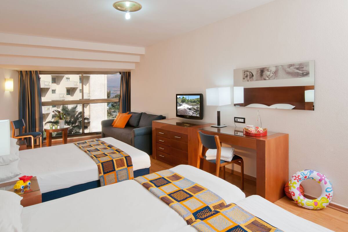 Une chambre d’hôtel avec deux lits, un bureau, une télévision et une vue sur les bâtiments environnants.