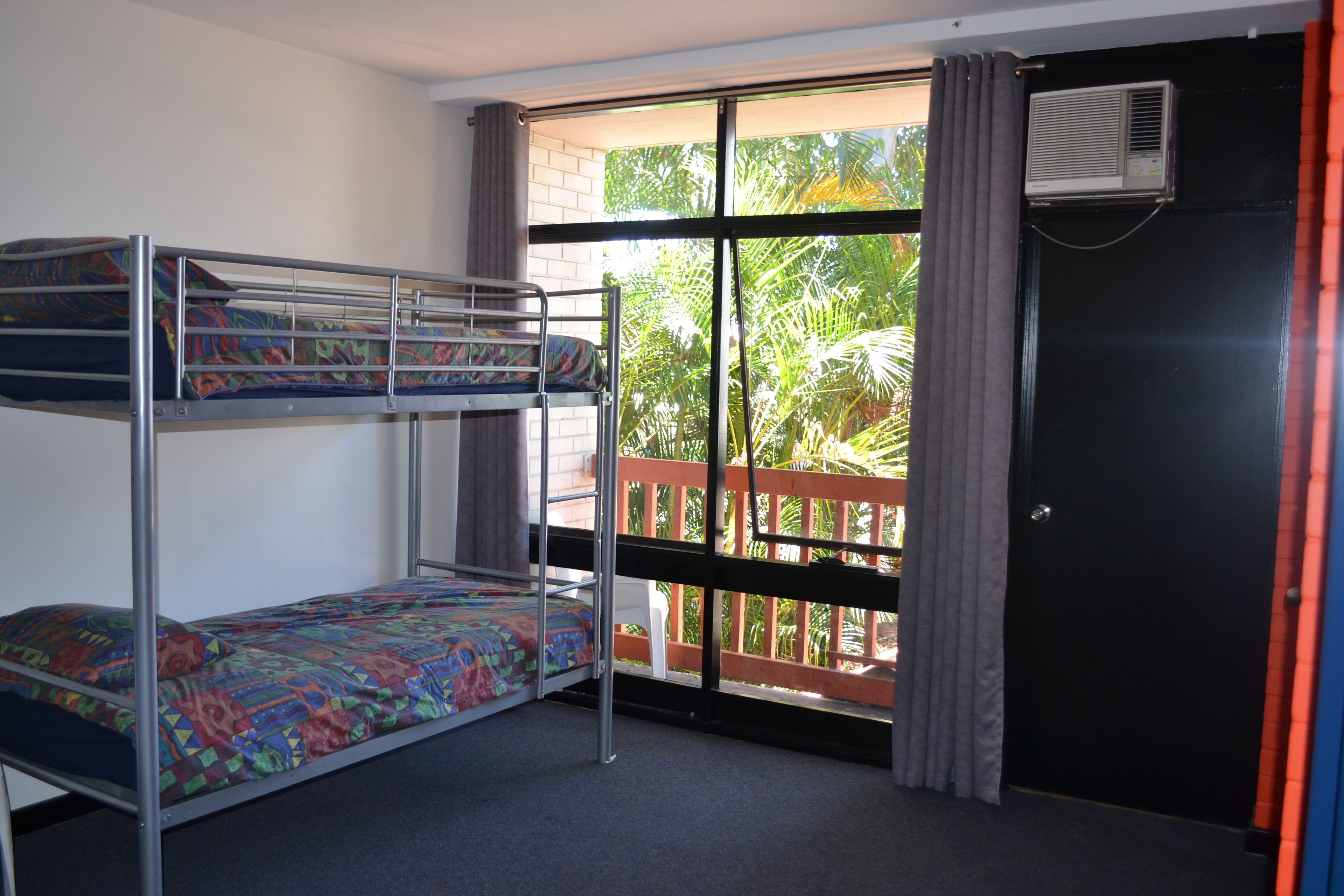 A dormitory room with bunk beds, a window with curtains, and an air conditioning unit.
