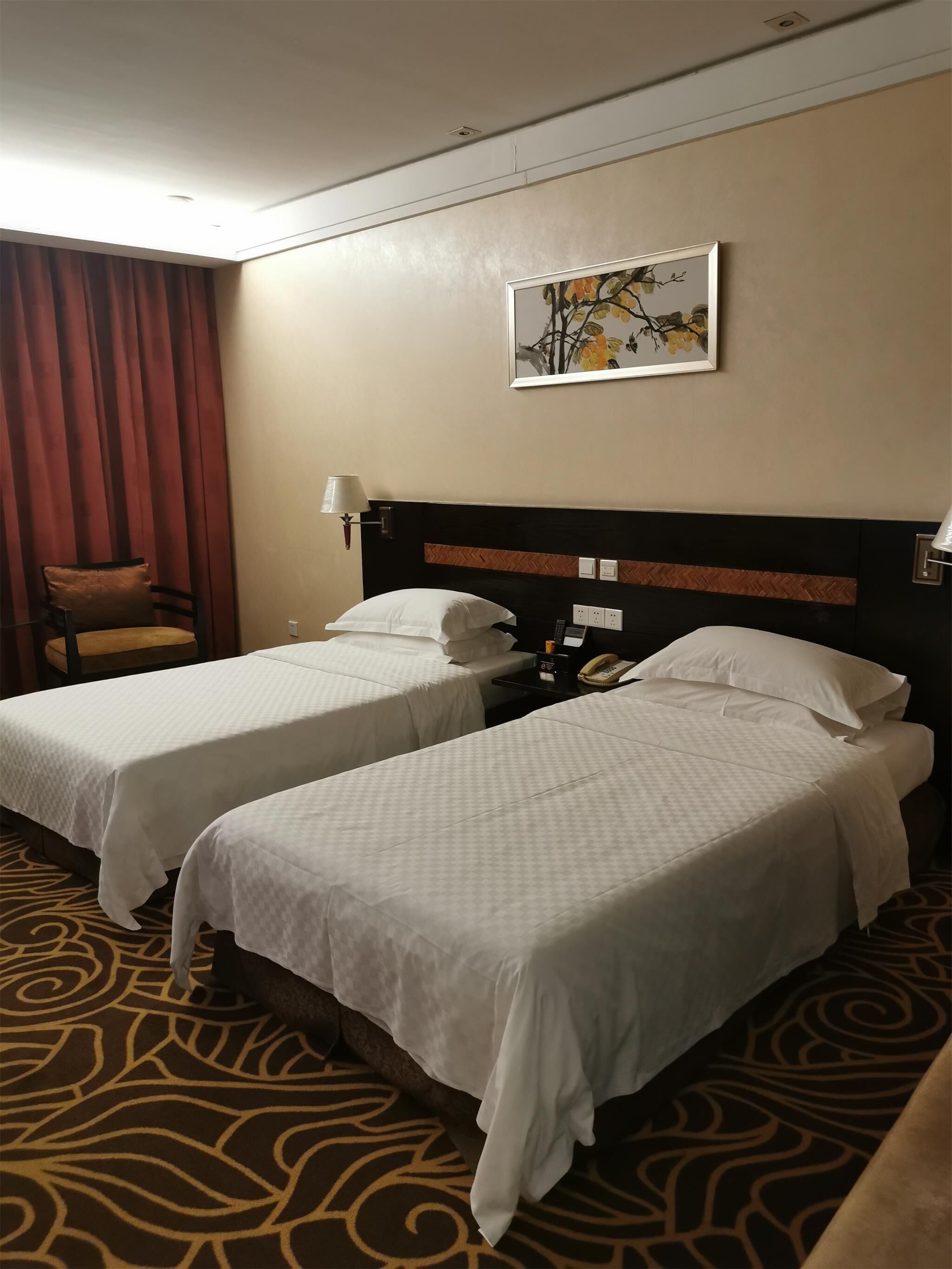 A hotel room with two beds, a headboard with a herringbone pattern, a wall-mounted telephone, and a painting of a tree branch.