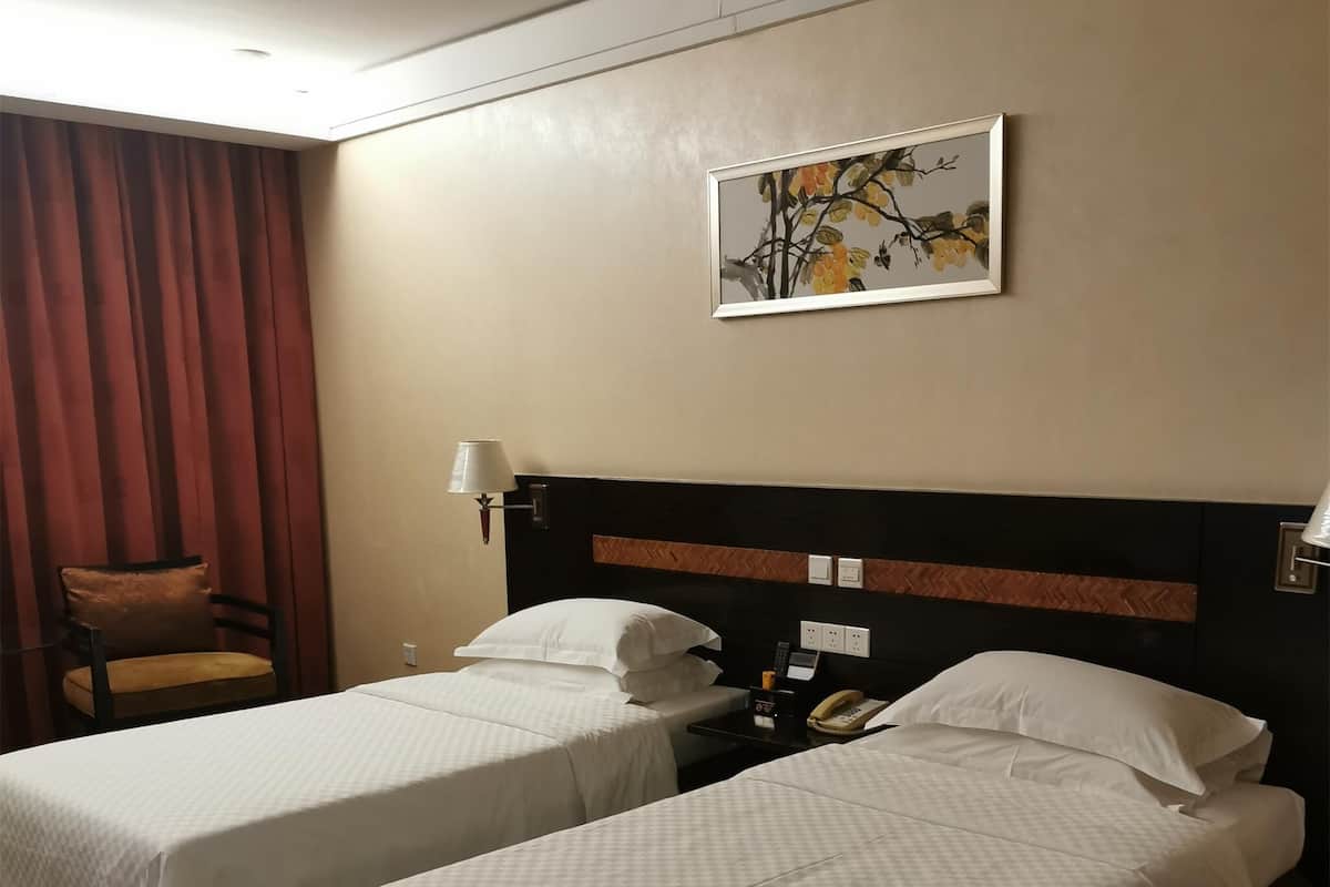 A hotel room with two beds, a headboard with a herringbone pattern, a wall-mounted telephone, and a painting of a tree branch.