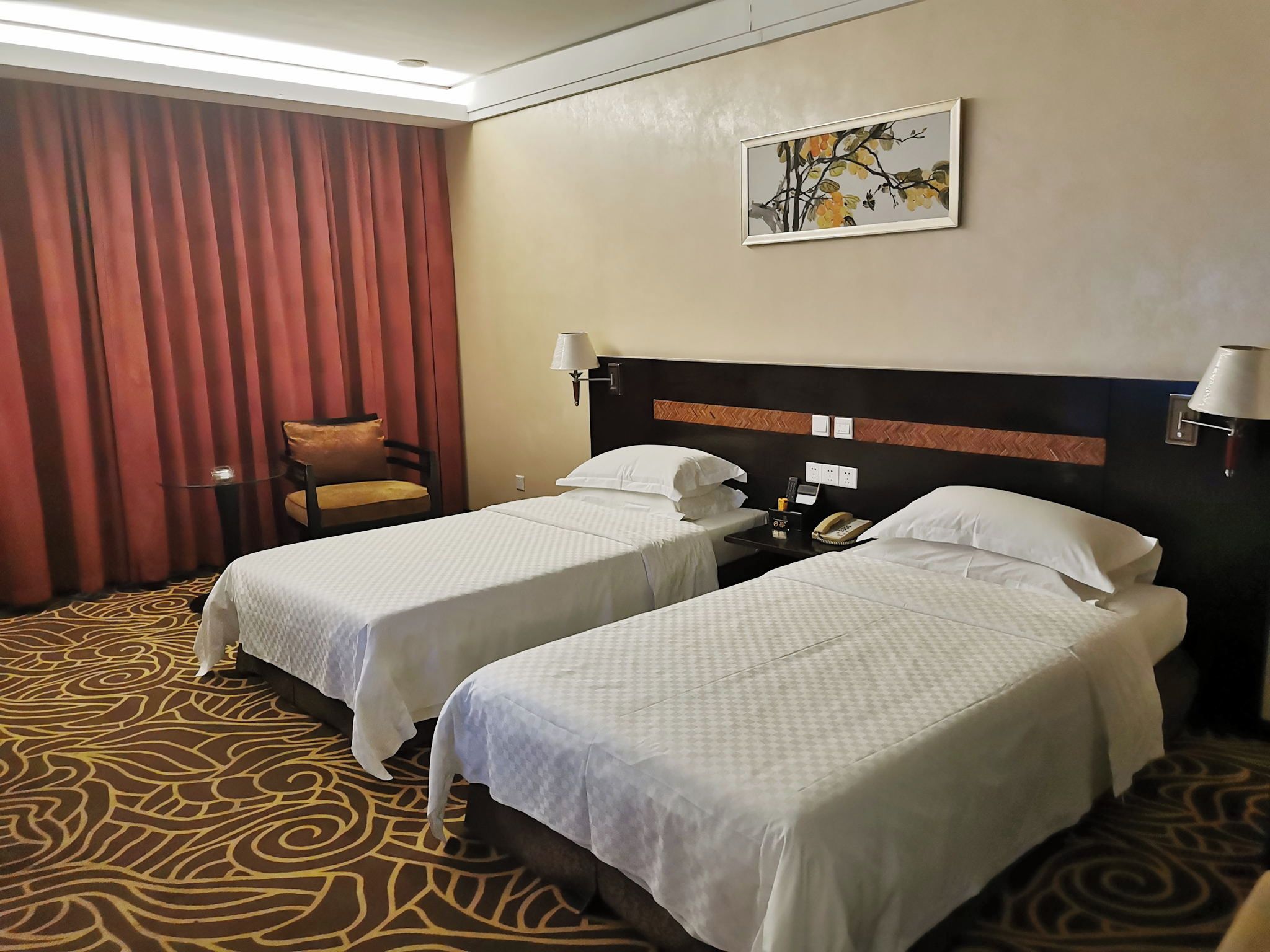 Habitación de hotel con dos camas, una silla, un cuadro en la pared y una alfombra estampada.