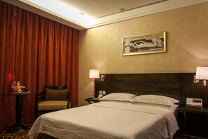 A hotel room with a bed, a chair, a table with fruit, a painting, and a nightstand with a lamp. - Huashi Hotel (Guangzhou)