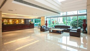 A spacious lobby with a reception desk, seating area, and large windows offering a view of greenery outside. - Huashi Hotel (Guangzhou)