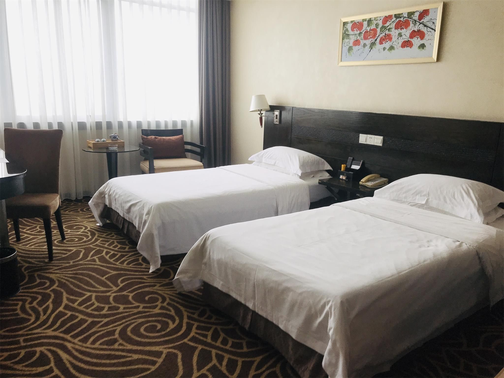 Habitación de hotel con dos camas, una mesita, una silla, una lámpara y un cuadro en la pared.