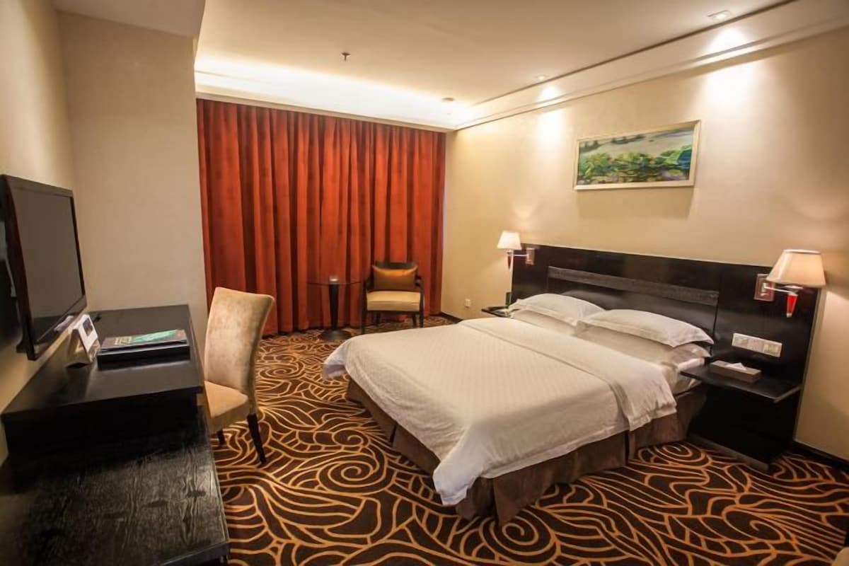 Una camera d'albergo con un letto, una scrivania, una sedia, una televisione e un quadro appeso al muro.