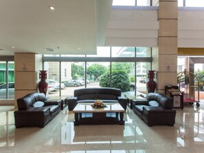 A lobby with a glass partition, leather sofas, a coffee table, and a vase with flowers. - Huashi Hotel (Guangzhou)