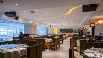 Un restaurante con varias mesas y cabinas, una cocina al fondo y vistas al exterior a través de amplias ventanas.