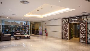 A spacious lobby with a modern design, featuring a seating area with sofas and a coffee table, a glass storefront, and a decorative wooden partition. - Huashi Hotel (Guangzhou)
