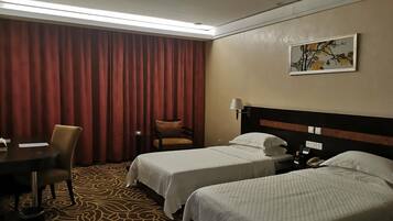 Quarto de hotel com duas camas, uma escrivaninha, uma cadeira, um abajur e um quadro na parede.