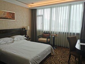 A hotel room with a large bed, a chair, a small table, and a window with sheer curtains. - Huashi Hotel (Guangzhou)
