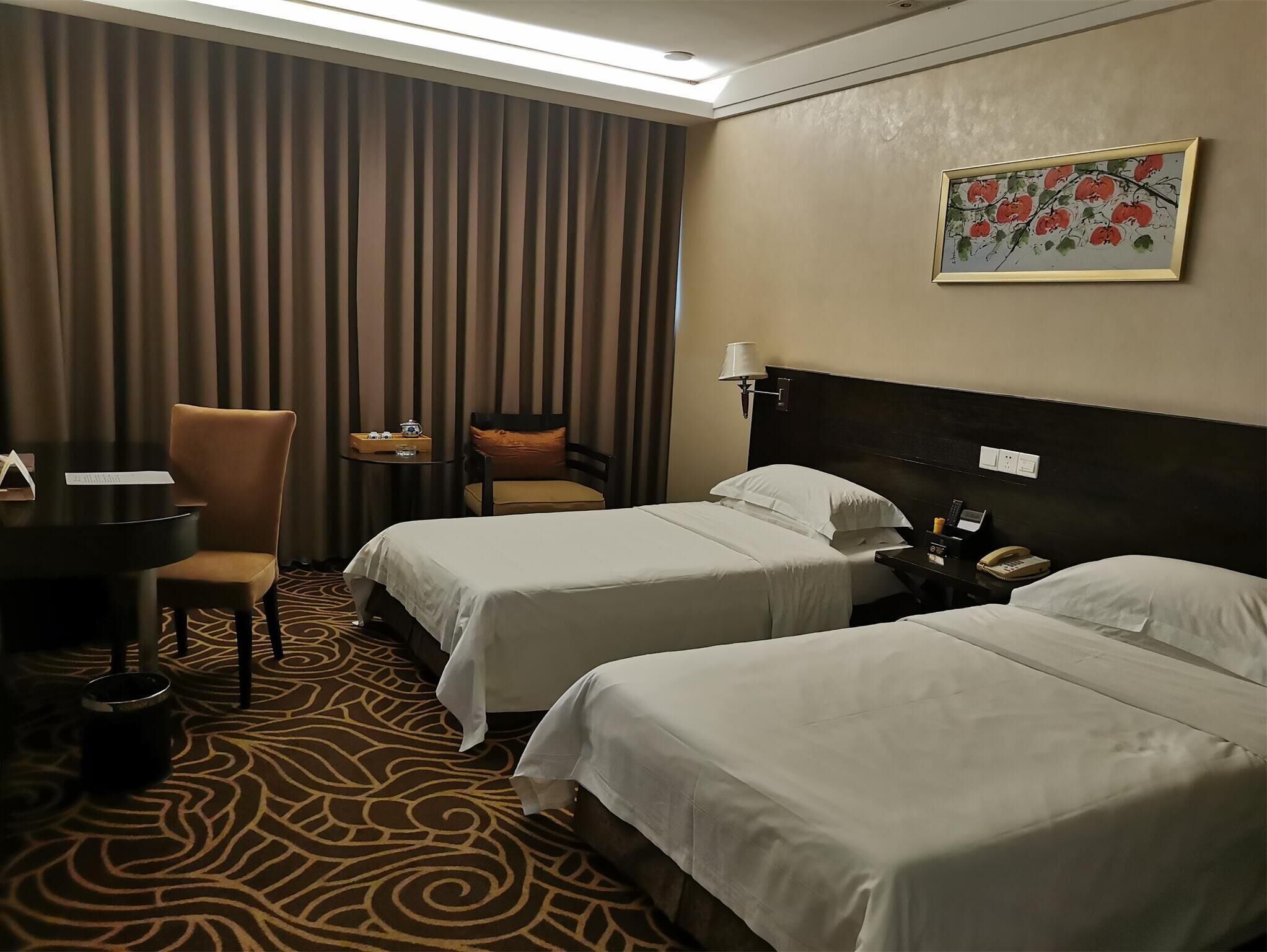 A hotel room with two beds, a desk, a chair, a small table, and a painting on the wall.