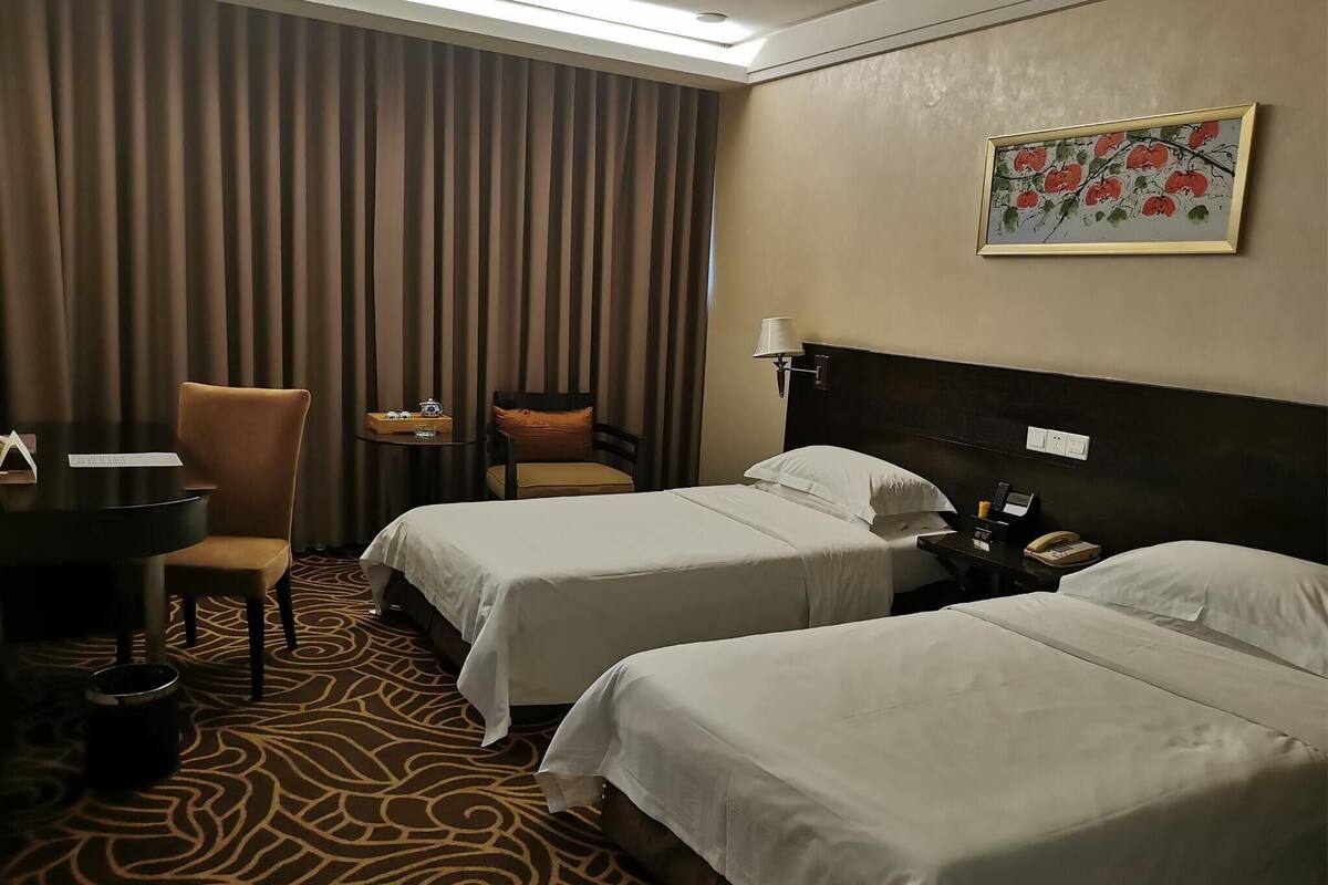 A hotel room with two beds, a desk, a chair, a small table, and a painting on the wall.