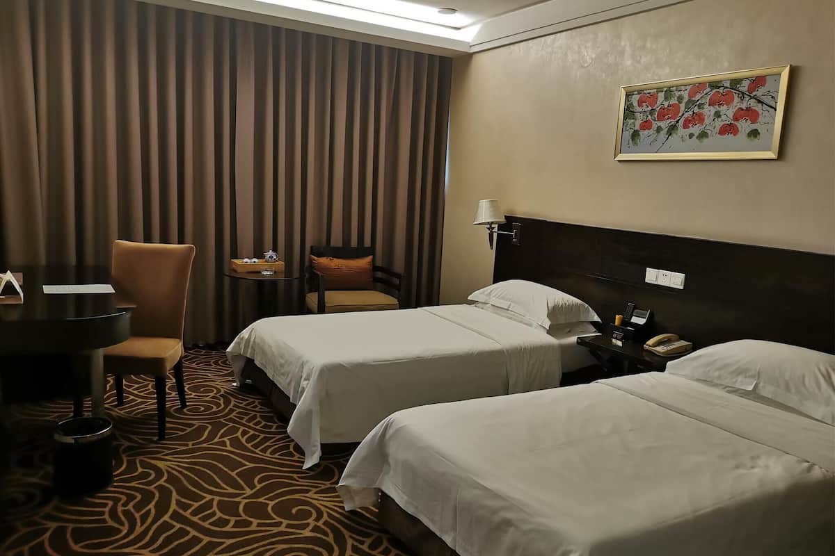 A hotel room with two beds, a desk, a chair, a small table, and a painting on the wall.