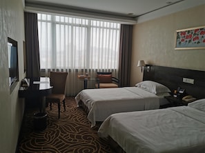 Camera d'albergo con due letti, una scrivania, una sedia, un tavolo e un'ampia finestra con tende.