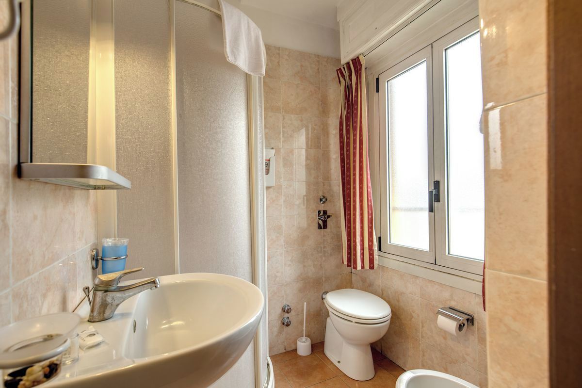 Un bagno con lavandino, water, doccia e una finestra con tenda.
