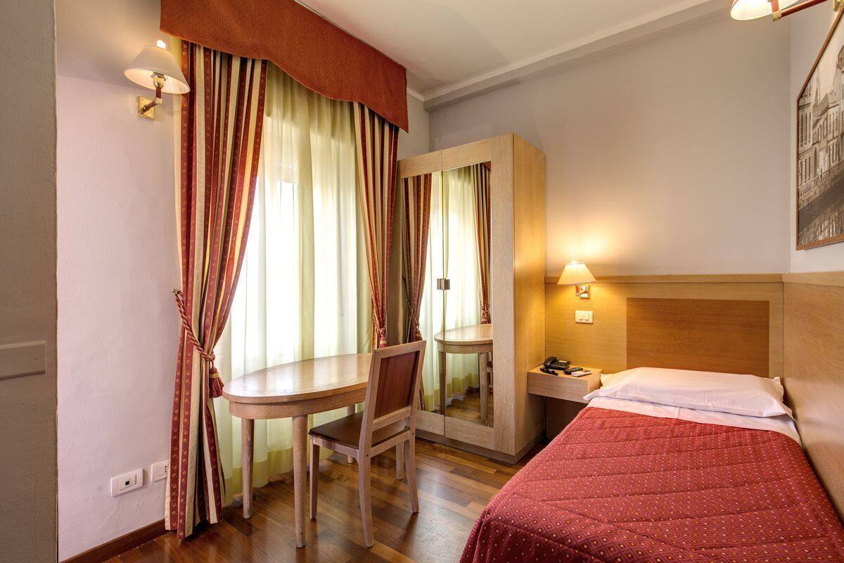 A hotel room with a bed, a desk, a chair, a mirror, and a nightstand.