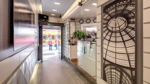 A corridor with a glass wall featuring a geometric pattern, a clock, and a plant. - Hotel Rio (Milan)