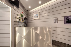 Una zona de bar con mostrador metálico, estanterías con botellas y un cuadro enmarcado en la pared.