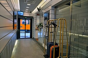 A hotel lobby with a luggage trolley, a glass wall with a view, and a door leading to a room. - Hotel Rio (Milan)