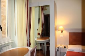 A hotel room with a bed, a bedside table with a lamp, a chair, a small table, and curtains. - Hotel Rio (Milan)