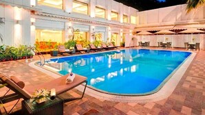 Una piscina con lettini e ombrelloni, circondata da un edificio con ampie finestre e pavimento piastrellato.
