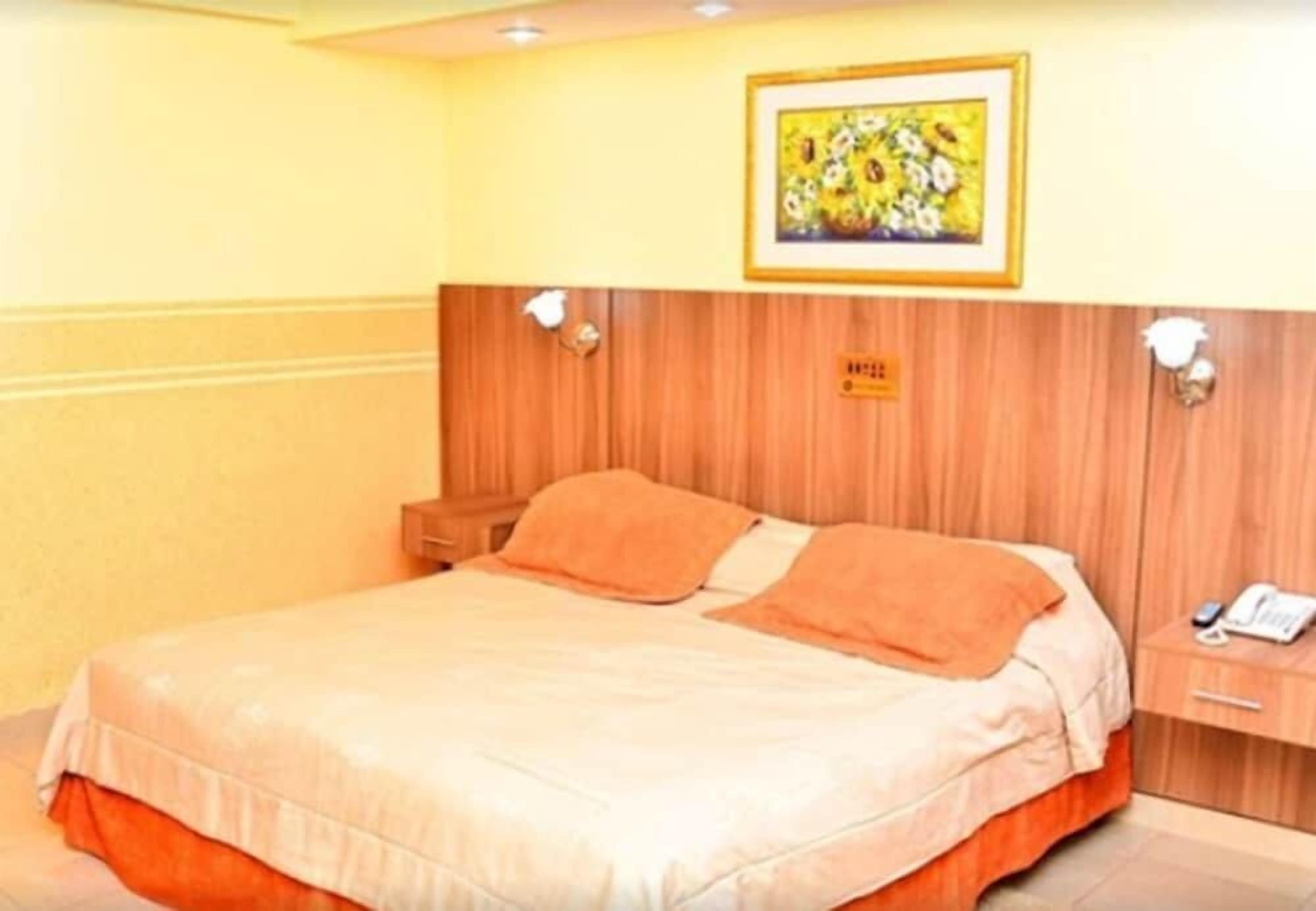 A hotel room with a bed, a nightstand, and a framed picture on the wall.