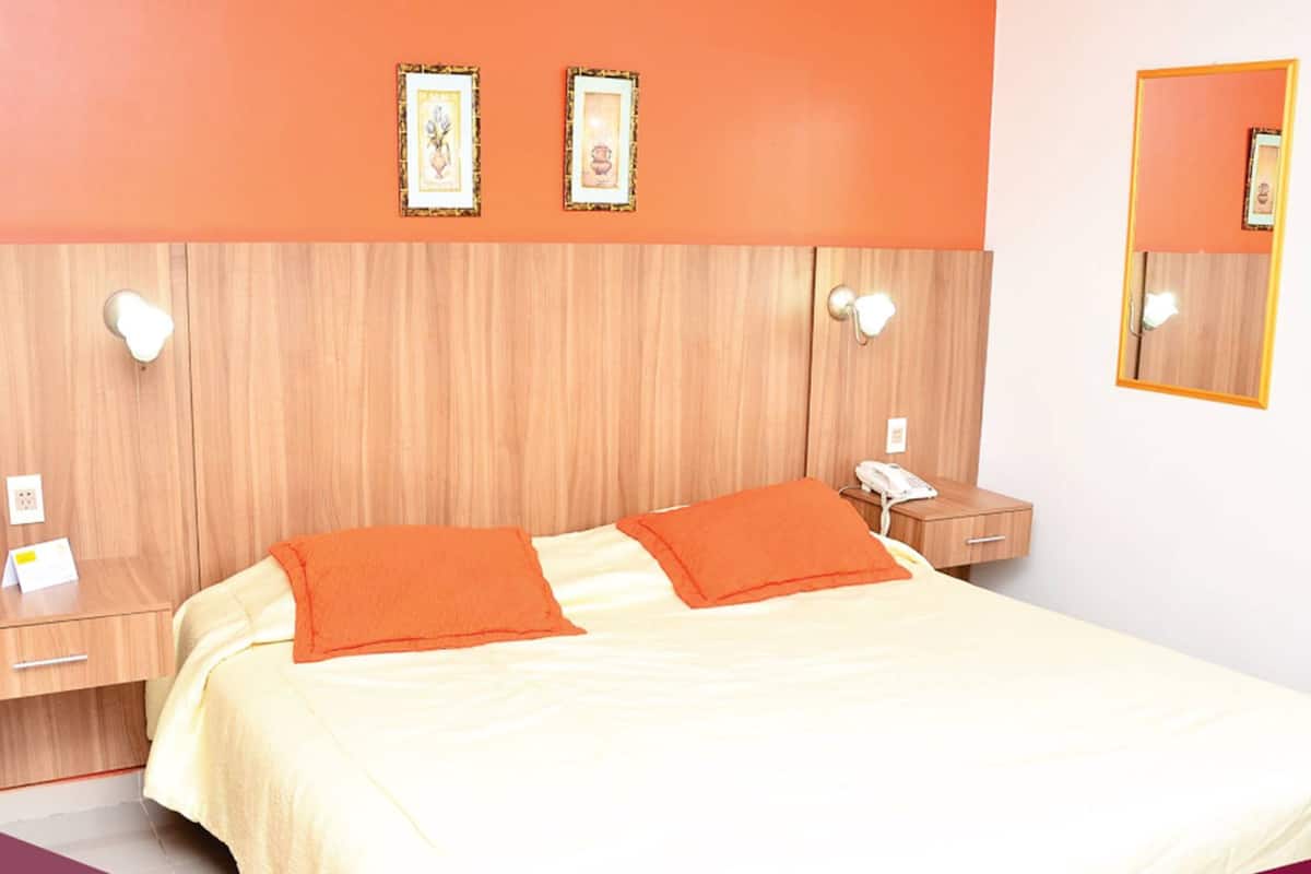 Una habitación de hotel con una cama, dos mesitas de noche, un teléfono y un espejo.
