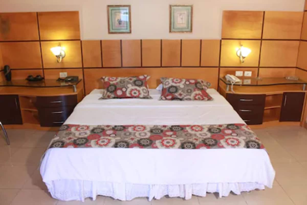 Una habitación de hotel con una cama grande, dos mesitas de noche, un escritorio y una silla.