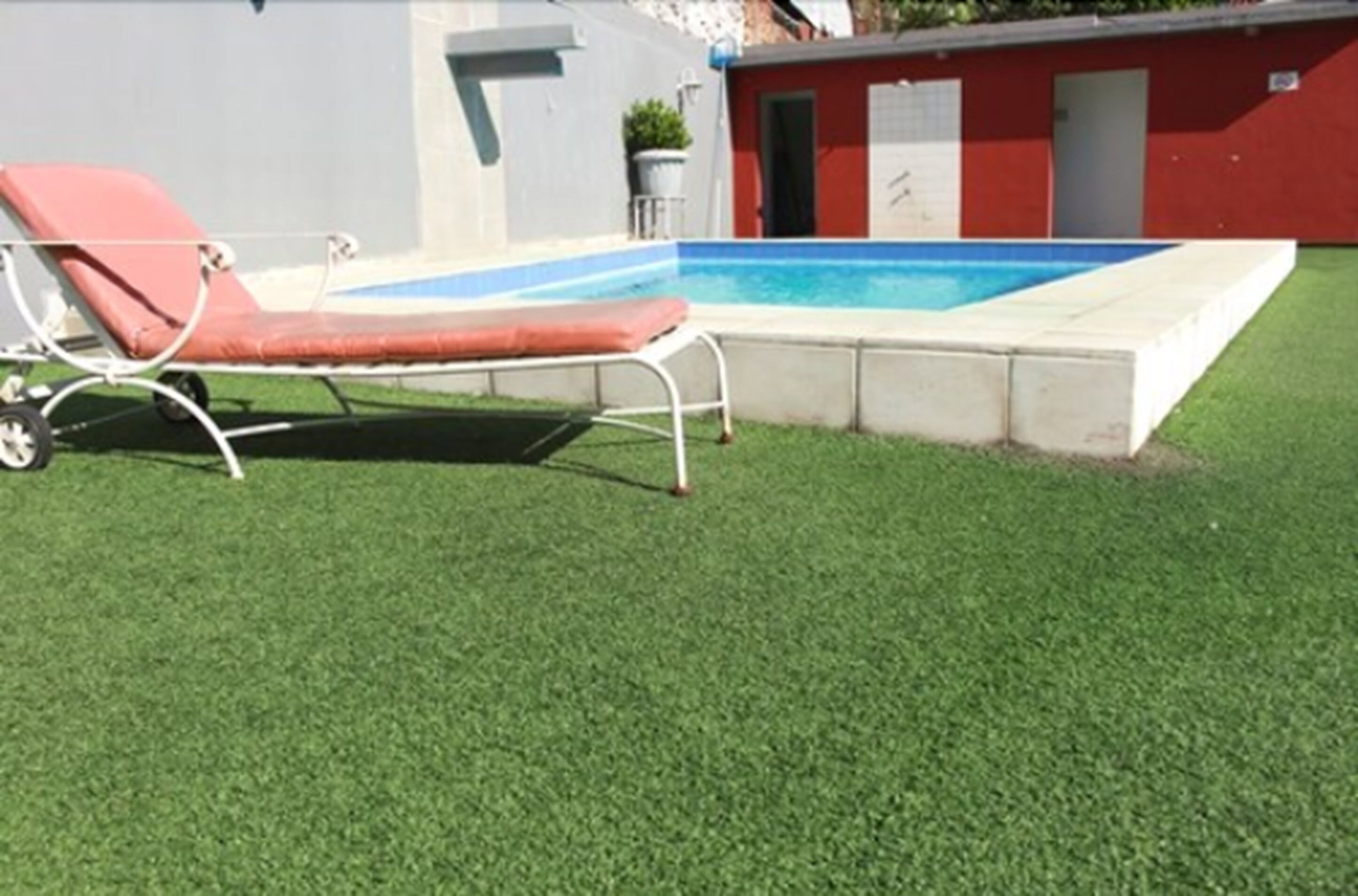 A swimming pool with a red lounge chair and a small shed in the background.